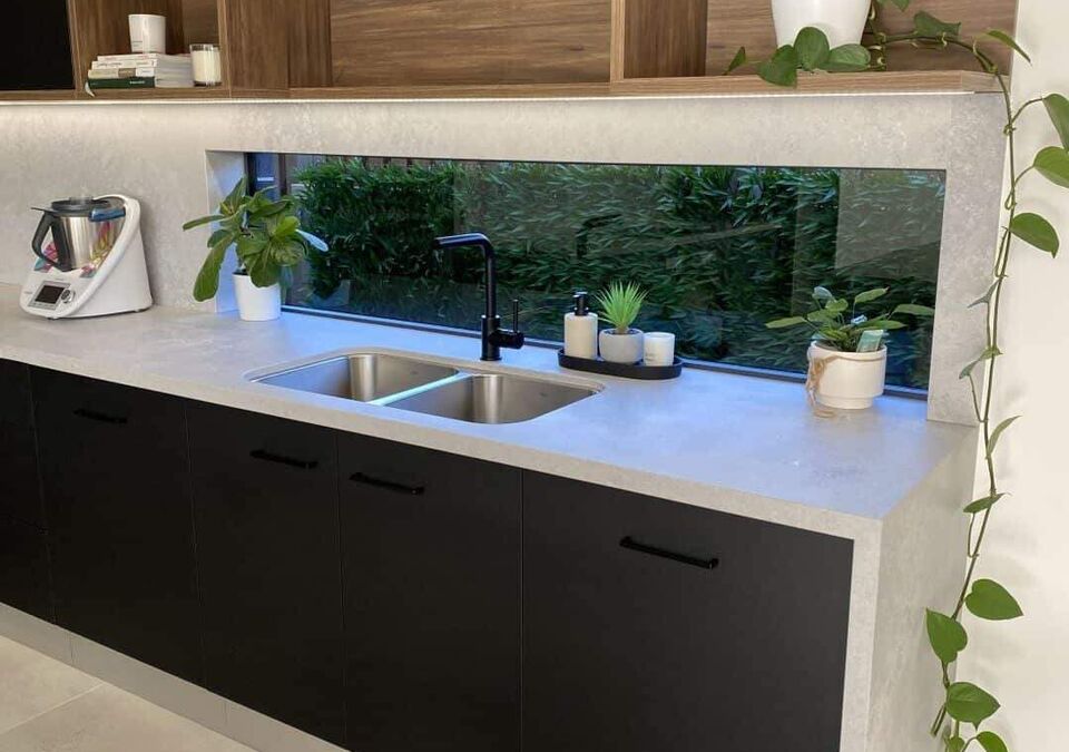 A dark kitchen with a stone benchtop and open shelving