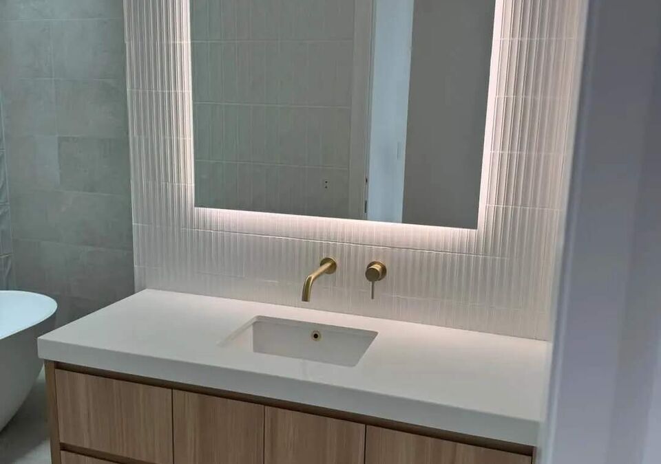A bathroom vanity with a backlit arched mirror