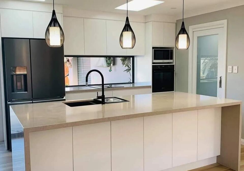 A white kitchen with a stone island and pendant lights