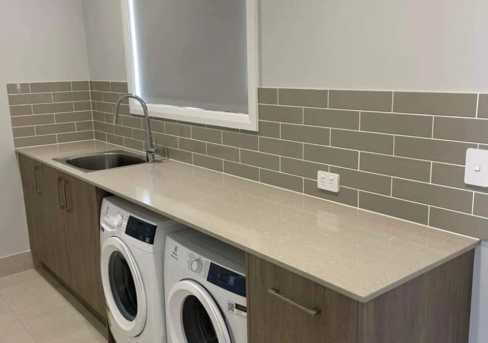 A laundry with a stone benchtop and tiled splashback
