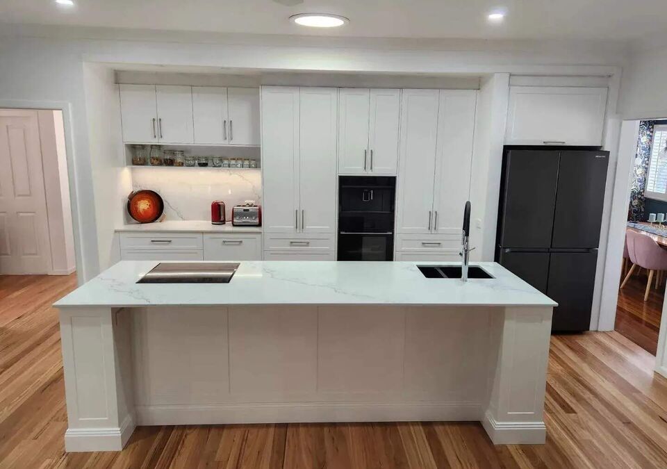 A white kitchen with a stone island and timber flooring