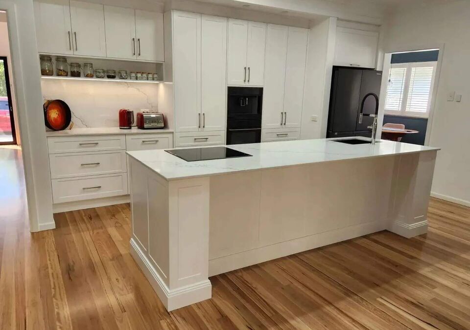 A white kitchen with a stone island viewed from the living area