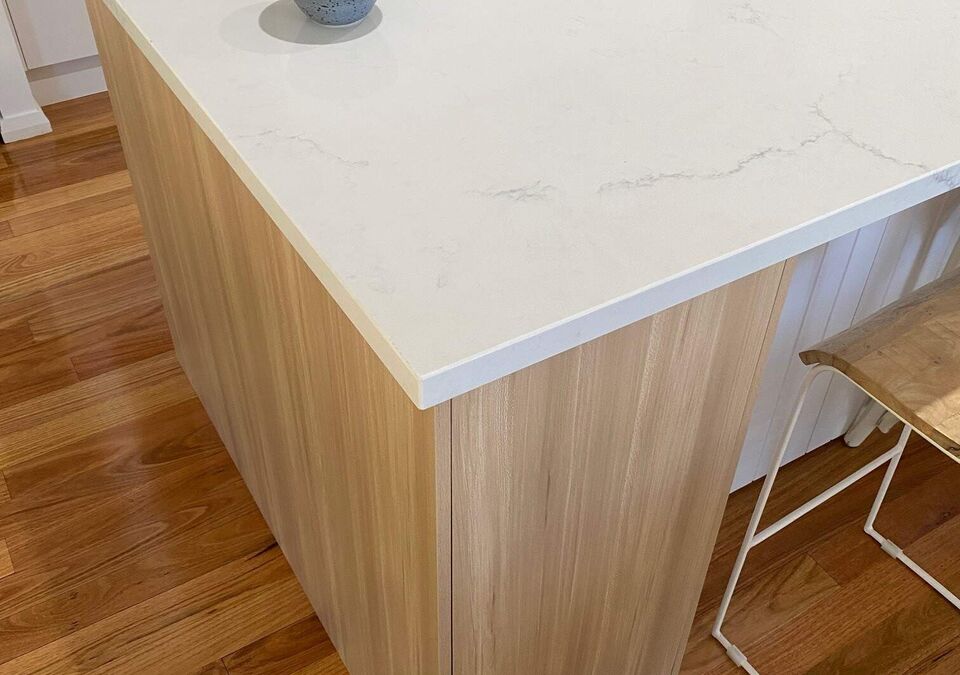 A white stone kitchen island beside timber cabinetry