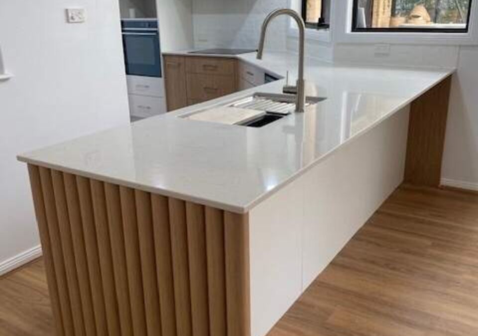 A modern kitchen with a white stone island and timber detailing