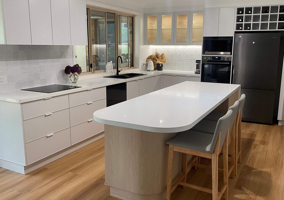 A white kitchen with a curved stone island